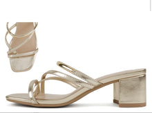 Cargar imagen en el visor de la galería, A pair of metallic gold heeled sandals with criss-cross straps and a block heel, shown on a plain white background with a smaller inset view of the sandal from the back.

